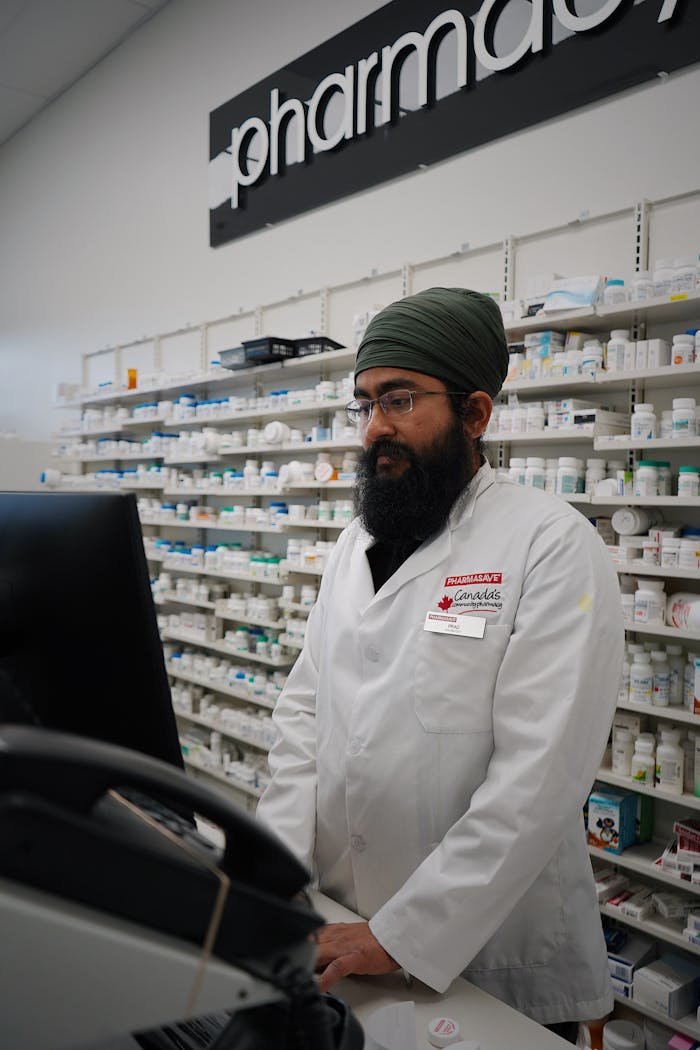 Asian male pharmacist in a lab coat working at a pharmacy counter with shelves of medicine.